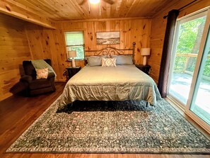 A wooden cabin bedroom with a bed, a chair, a nightstand, and a window.