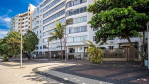 A multi-story building with balconies, a paved plaza with patterned tiles, and a tree-lined street. - Apartment With sea View in RJ Brt1001 (Rio de Janeiro)