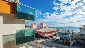 Un edificio costero con balcón de vidrio que da al mar, un edificio rosa con torre del reloj y un edificio azul con señalización.