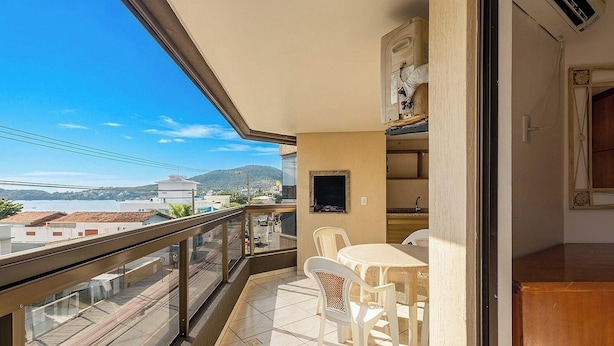 Un balcón con vistas al agua y colinas, un comedor con mesa y sillas, y una pequeña cocina.