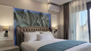 Ein Hotelzimmer mit einem rautenförmig geprägten Kopfteil, einem großen Bett mit weißen Leinen, einer türkisfarbenen gesteppten Tagesdecke, einer wandmontierten Klimaanlage und einem Fenster mit Vorhängen.