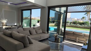 Ein modernes Wohnzimmer mit einem Ecksofa, einem Glastisch und Blick auf einen Swimmingpool.