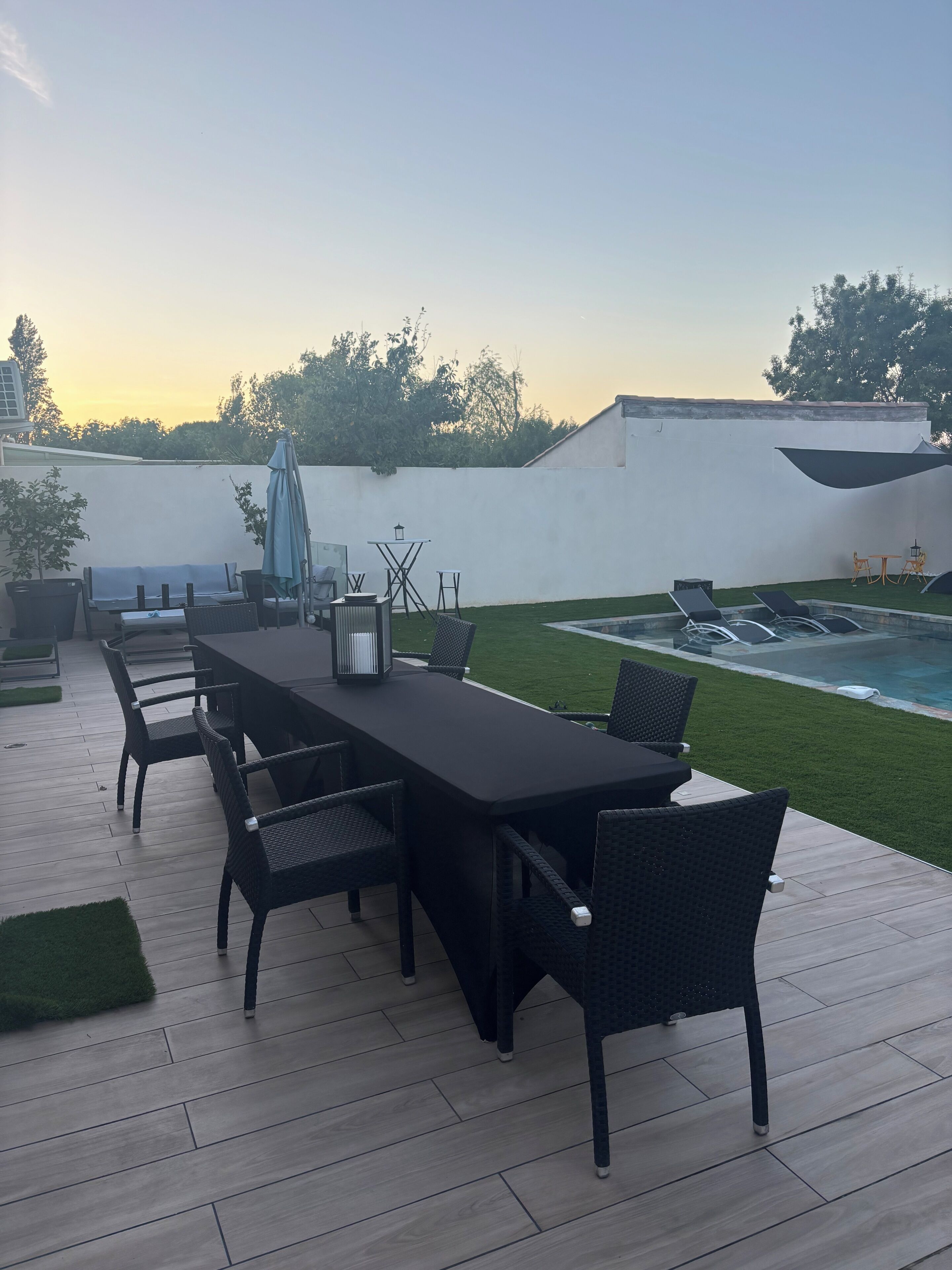 Une terrasse avec une table et des chaises, une piscine et un mur blanc.