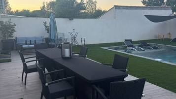 Une terrasse avec une table et des chaises, une piscine et un mur blanc.