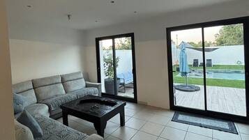 Un salon moderne avec un canapé, une table basse et une porte-fenêtre coulissante donnant sur une terrasse.