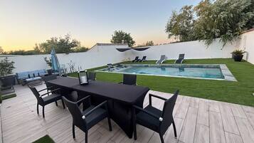 Un espace aménagé au bord de la piscine, avec une table et des chaises, une piscine et un mur blanc.