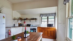 Una cocina con armarios blancos, encimera de madera, estufa, microondas y ventana con un valance a cuadros.