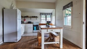 Una cocina con refrigerador blanco, mesa de madera y banco, con una ventana y una puerta a la vista.