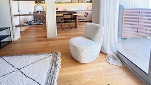 Ein modernes Wohnzimmer mit großem Fenster, einem gemütlichen Sessel, einem Holztisch und einem Teppich.