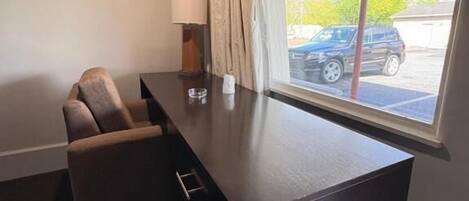 Une pièce avec un bureau en bois foncé, une chaise, une lampe et une fenêtre avec des rideaux.
