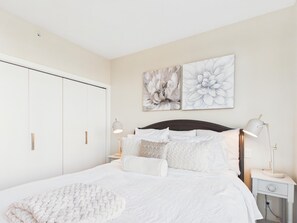 A bedroom with a bed, nightstands, a wardrobe, and two wall-mounted paintings.