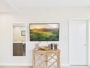 A modern living room with a flat-screen TV mounted on the wall, a wooden console table with books and decorative items, and a view into the adjacent bathroom. - Chic Urban Sanctuary in Downtown Victoria (Victoria)