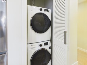 A wall-mounted washer and dryer unit with a control panel, located in a room with a wooden floor and a door with horizontal louvered panels.
