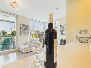 A bottle of wine and a wine glass on a table in a well-lit room with a view of buildings through large windows. - Chic Urban Sanctuary in Downtown Victoria (Victoria)