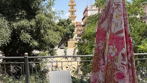 A balcony with a metal railing, a patterned umbrella, and a tower in the background.