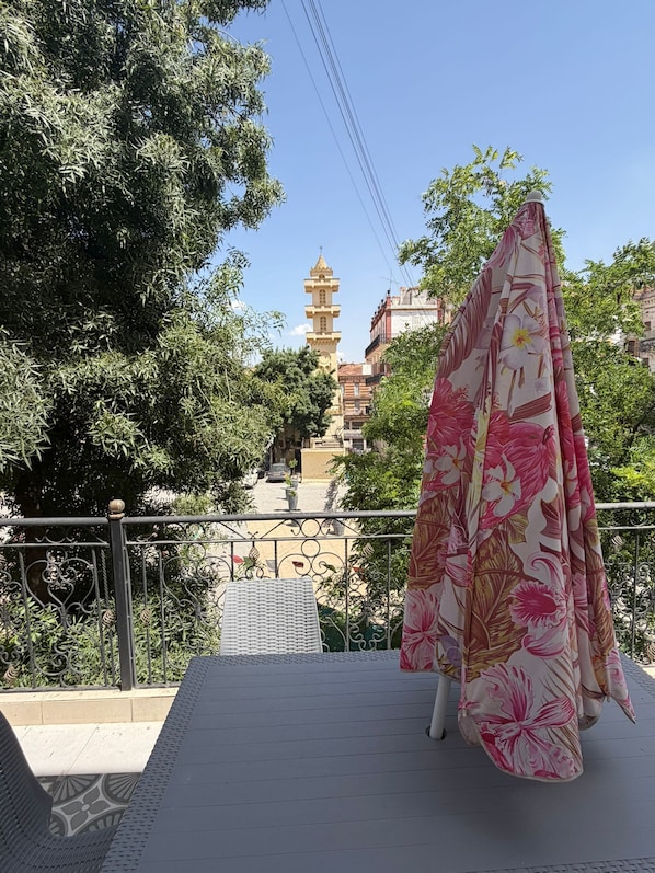 A balcony with a metal railing, a patterned umbrella, and a tower in the background.