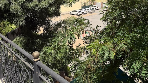 A view of a building with a tower, surrounded by trees and parked cars.