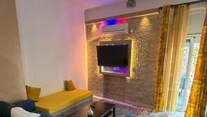 A modern living room with a sectional sofa, a coffee table, and a flat-screen TV mounted on a textured wall.