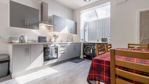 Een compacte keuken met grijze kastjes, een wasmachine en een eethoek met een rood geruit tafelkleed.