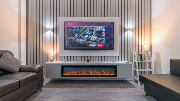 Een moderne woonkamer met een flatscreen televisie aan de wand, een ingebouwde open haard en een bank.