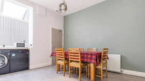 Een keuken met een wasmachine, een eettafel met stoelen en een radiator.