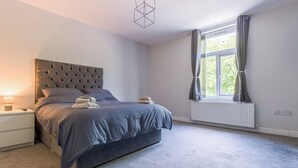Een slaapkamer met een bed, nachtkastje, lamp, raam met gordijnen en een radiator.