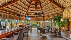 A covered outdoor seating area with a bar, wicker furniture, and a ceiling fan. - 601 Monroe Ave (Cape Canaveral)