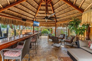 A covered outdoor seating area with a bar, wicker furniture, and a ceiling fan. - 601 Monroe Ave (Cape Canaveral)