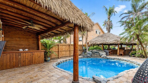 A pool area with a wooden deck, a thatched-roof structure, and a stone wall. - 601 Monroe Ave (Cape Canaveral)