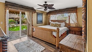 A bedroom with a bed, a ceiling fan, a nightstand, a wicker chair, a wooden floor, and a view of a garden through a sliding glass door. - 601 Monroe Ave (Cape Canaveral)