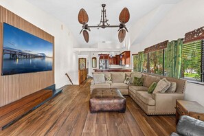 A spacious living room with a large sectional sofa, a wooden coffee table, and a large painting of a pier. - 601 Monroe Ave (Cape Canaveral)