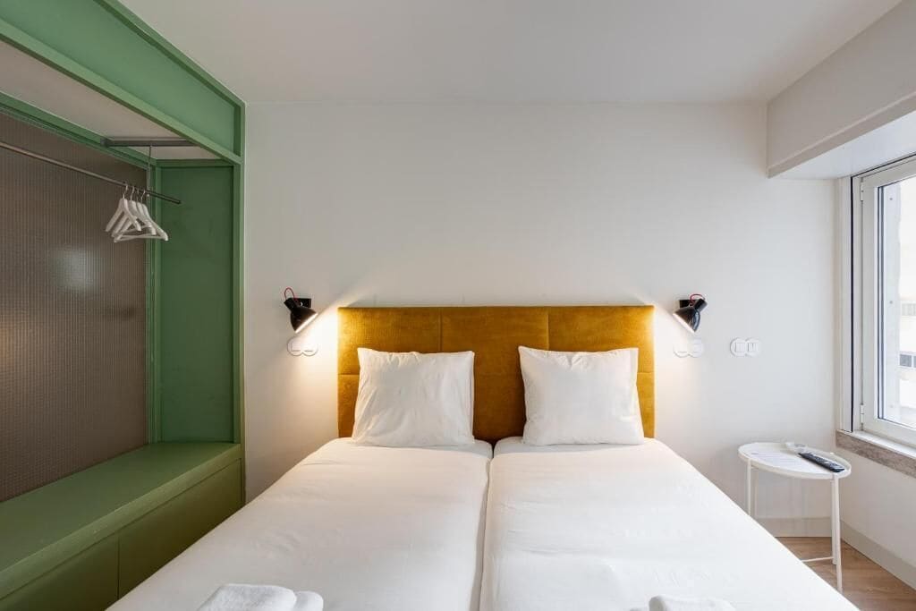 A hotel room with a bed, a bench, a small table, and a window.
