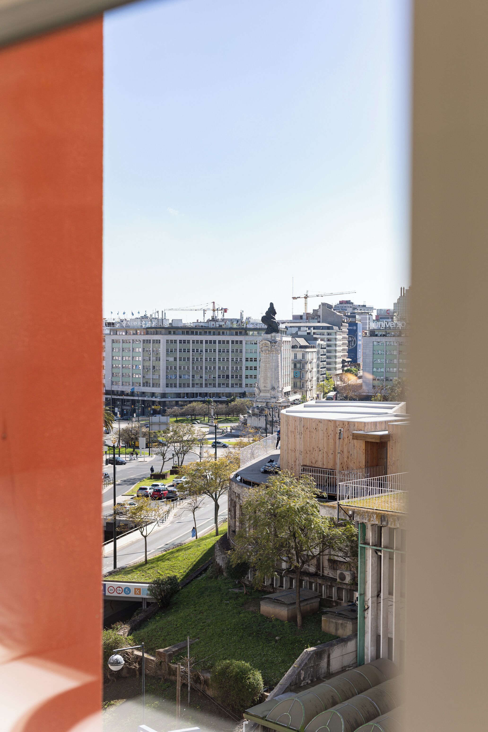 A view of a cityscape with buildings, a statue, and a round structure with a green roof.