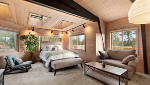 A cozy bedroom with a bed, bedside tables, a sofa, and a large window. - Tahoe Sanctuary | Hot Tub Sauna | Mountain & Lake Views | Air Conditioning (South Lake Tahoe)
