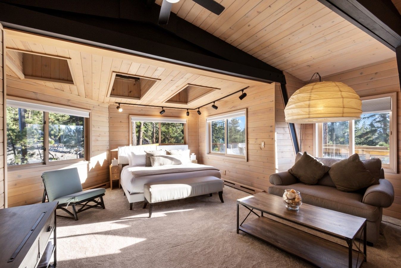 A cozy room with a bed, a sofa, a coffee table, and large windows offering a view of the outdoors.