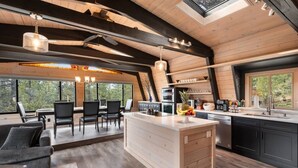A modern kitchen with a central island, wooden beams, and large windows. - Tahoe Sanctuary | Hot Tub Sauna | Mountain & Lake Views | Air Conditioning (South Lake Tahoe)