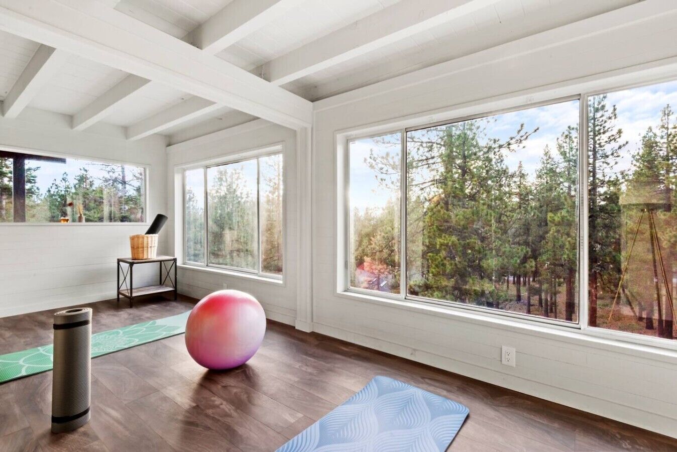 A spacious room with large windows, a yoga mat, a yoga ball, and a small table with a basket.
