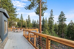 A wooden deck with lounge chairs, surrounded by tall pine trees.