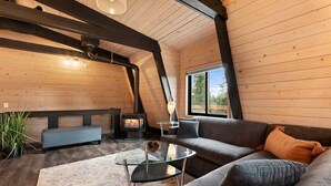 A cozy cabin interior with a sofa, a glass coffee table, a bench, and a wood-burning stove. - Tahoe Sanctuary | Hot Tub Sauna | Mountain & Lake Views | Air Conditioning (South Lake Tahoe)