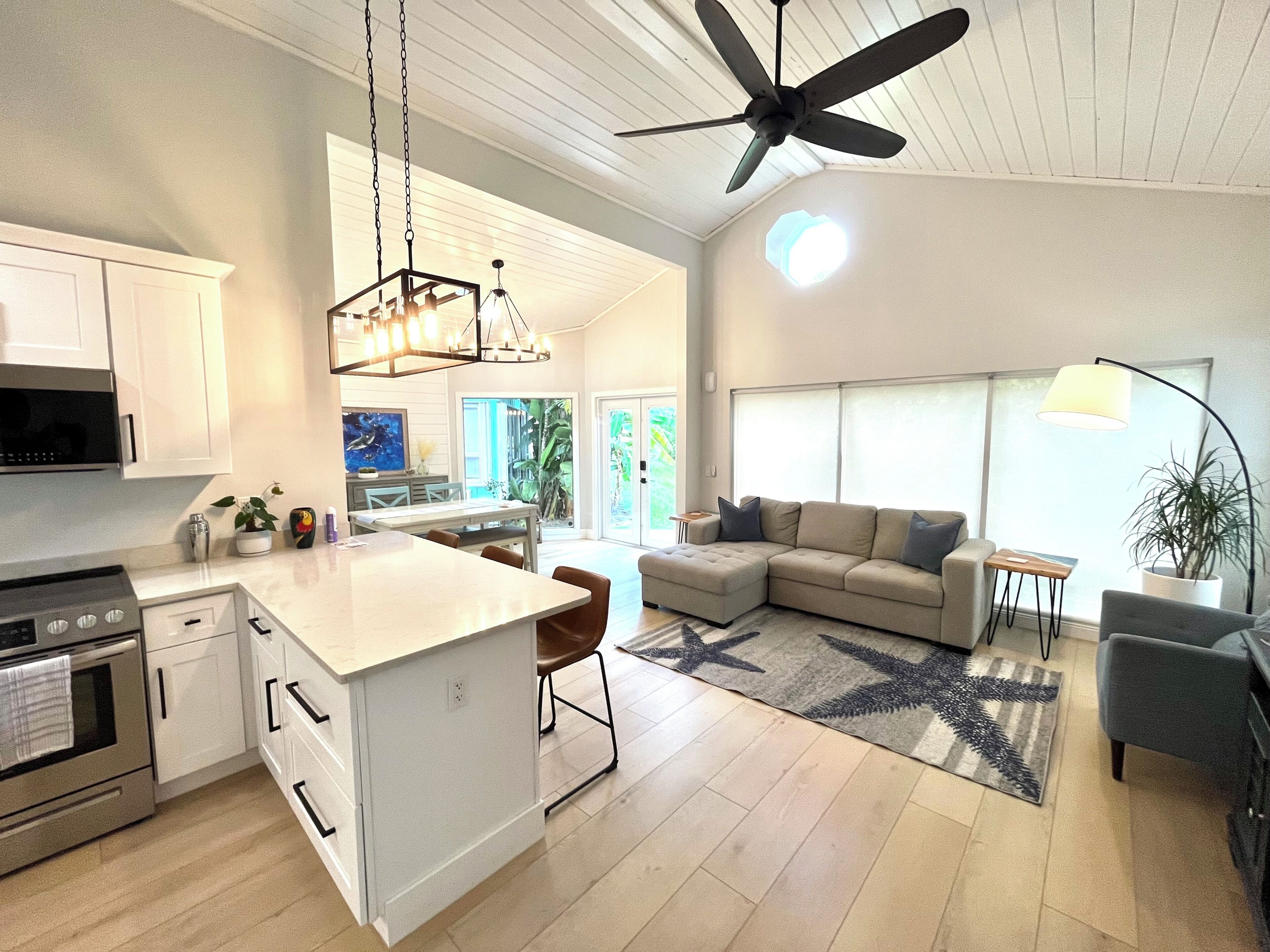 A modern kitchen with white cabinetry, a central island, a ceiling fan, and a dining area with a sofa and coffee table.