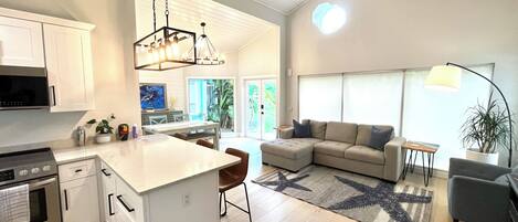 A modern kitchen with white cabinetry, a central island, a ceiling fan, and a dining area with a sofa and coffee table.