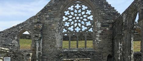 A historical building with a large arched window featuring a geometric pattern, stone columns, and a stone bench.