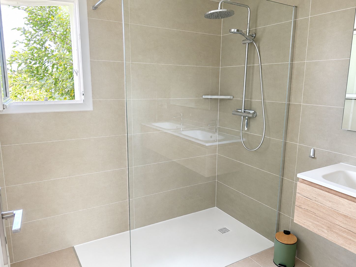 A modern bathroom with a glass-enclosed shower, a white sink, and a wooden floor.