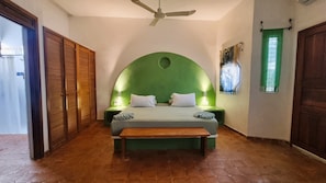 A bedroom with a green arch headboard, a wooden bench, two bedside lamps, and a ceiling fan.