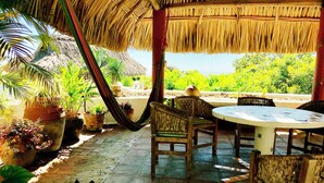 A covered outdoor seating area with a table and chairs, surrounded by potted plants and a thatched roof. - 3 bdrm house with Private Pool & Steps from Manzanillo Beach (Puerto Escondido, Oaxaca, Mexico)
