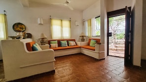 A living room with a sofa, a coffee table, a lamp, and a view through a door.