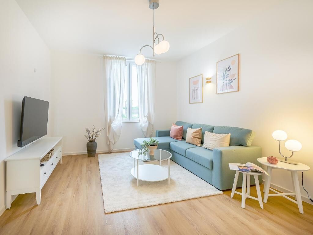 Un salon avec un canapé, une table basse, un téléviseur posé sur un meuble et une fenêtre avec des rideaux.