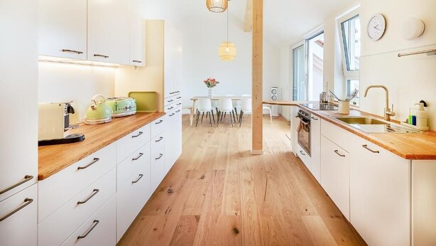 Una cocina moderna con armarios blancos, encimeras de madera e iluminación colgante.