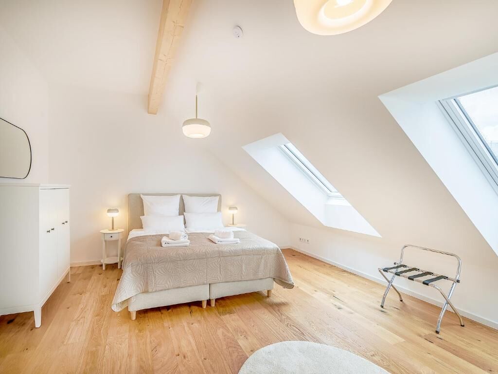 Une chambre à coucher comprenant un lit, des tables de chevet, un banc, une lucarne et une armoire.