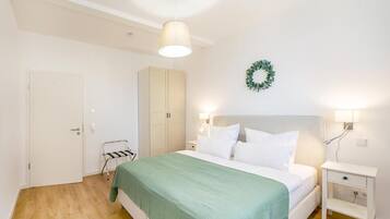 A bedroom with a bed, a nightstand, a wall-mounted light, a door, and a wardrobe.
